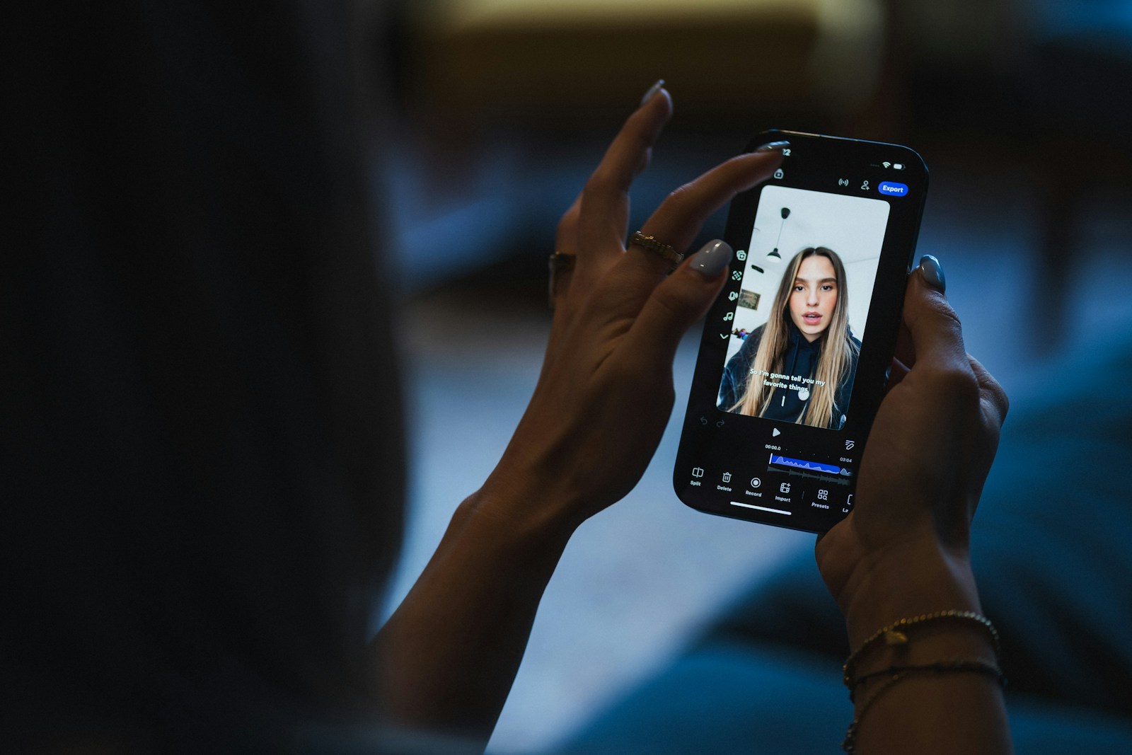 Close-up of hands holding a smartphone that plays a vertical video of a young woman talking, with a caption across the screen