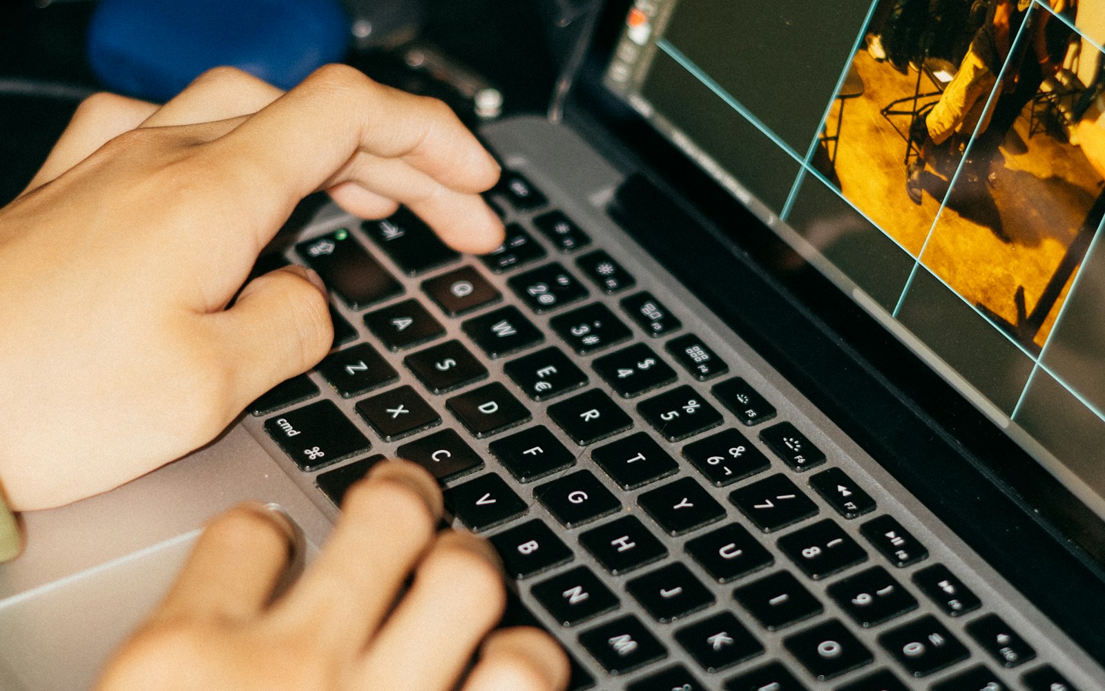 Close-up of two hands typing on a laptop keyboard while the screen beside them shows a warm-toned photo being cropped with a grid overlay