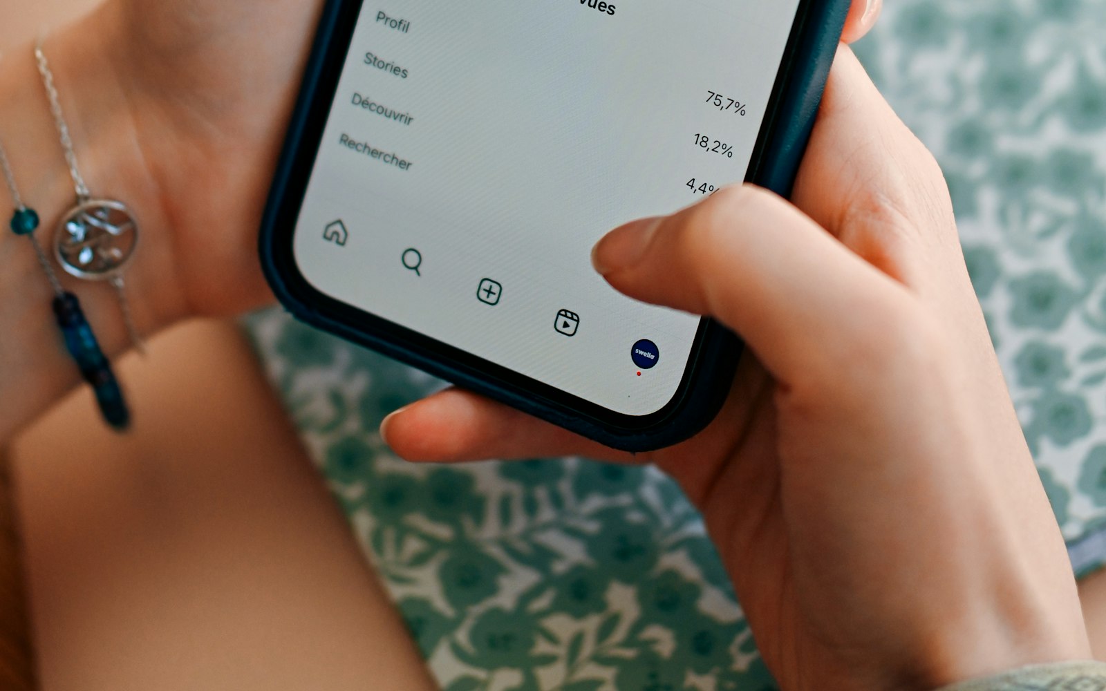 Close-up of hands holding a smartphone showing a breakdown of views in French, with Profil, Stories, Découvrir and Rechercher listed beside percentages such as 75.7% and 18.2%
