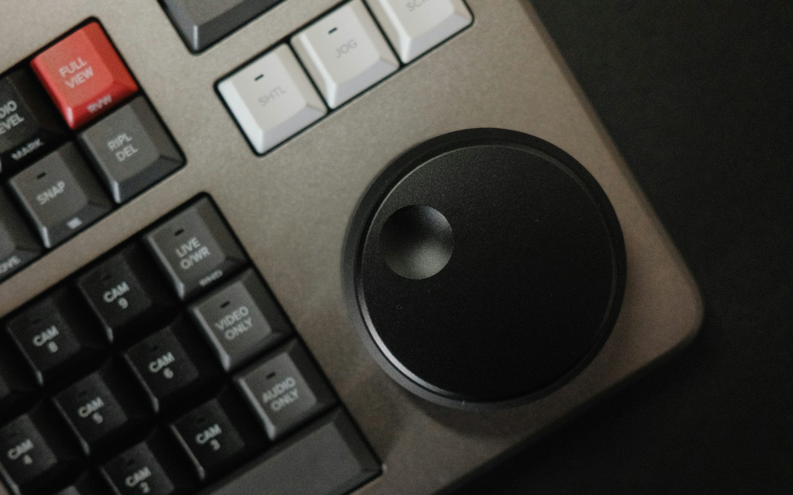 Close-up of a video editing control panel with labelled camera, live overwrite and audio buttons beside a large black jog wheel
