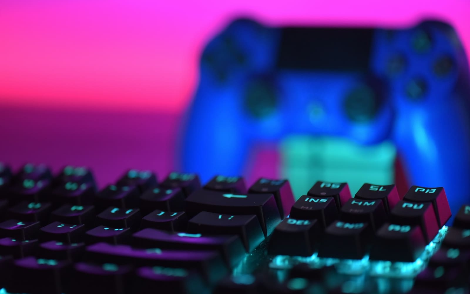 Close-up of black mechanical keyboard keys with cyan backlighting, a blurred blue game controller behind them against a bright pink background