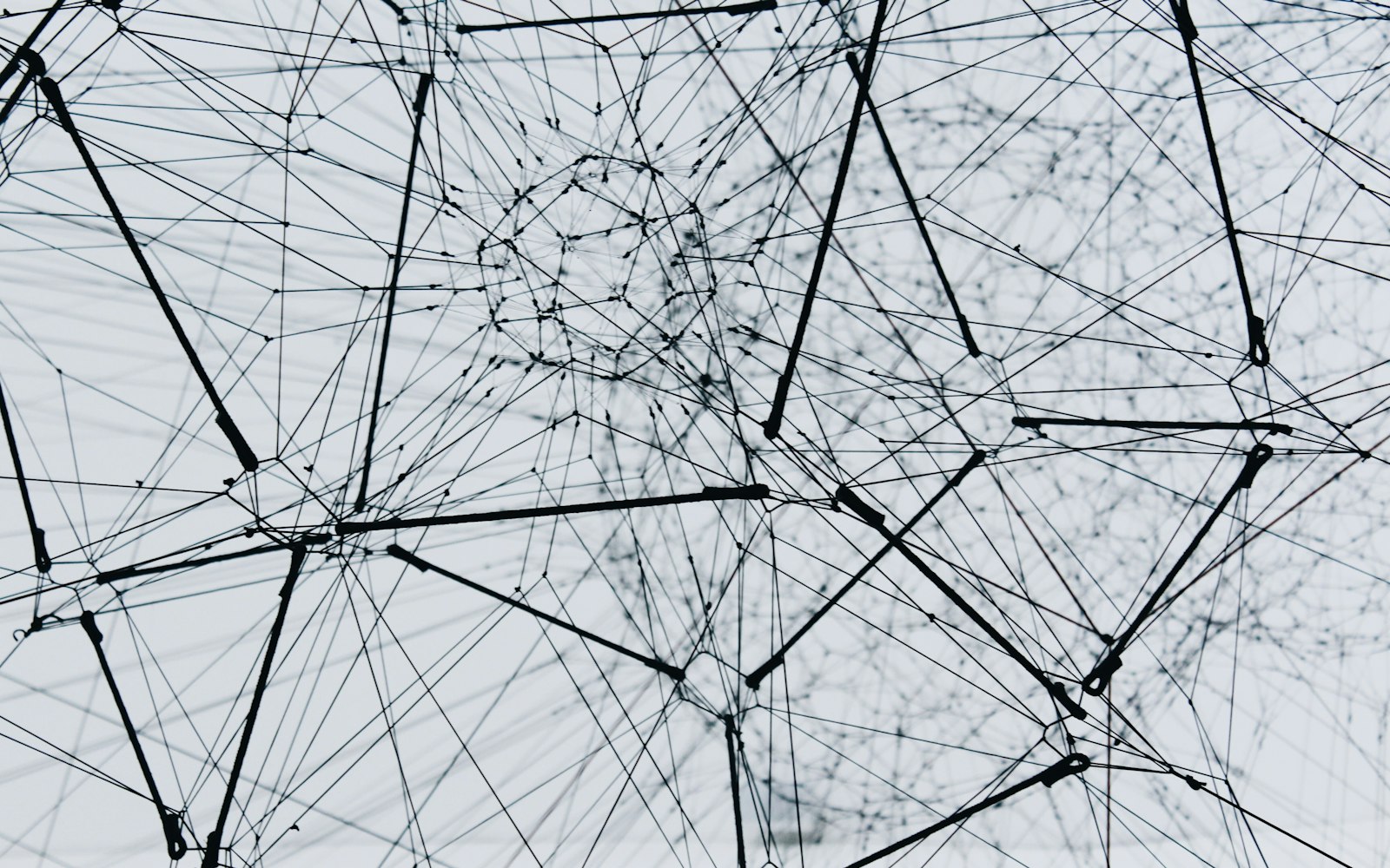 A dense web of black cords and knotted strings strung between poles against a pale sky, like the nodes and edges of a neural network diagram