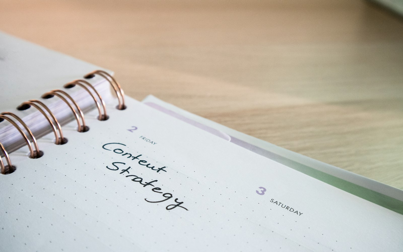 A spiral-bound weekly planner on a wooden desk, with Content Strategy handwritten in the Friday slot next to an empty Saturday